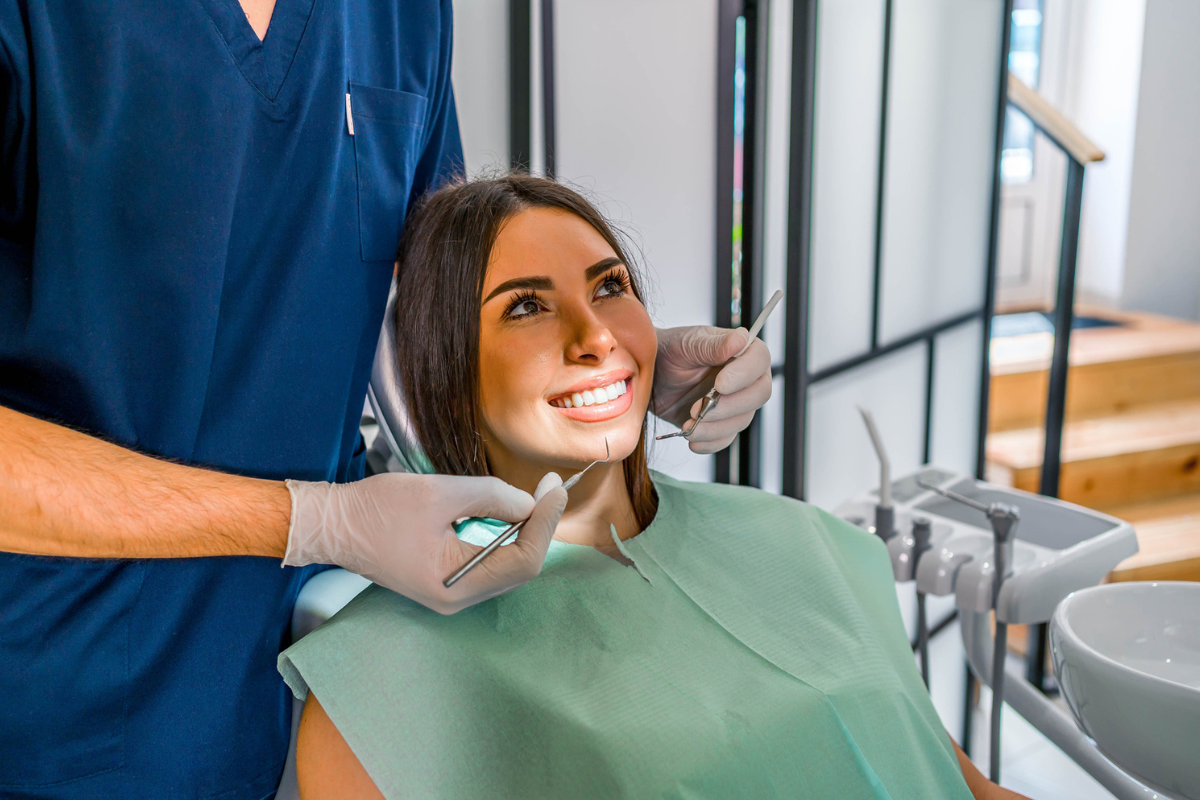 Woman smiling in dental chair with dentist holding dental mirror and explorer tools.