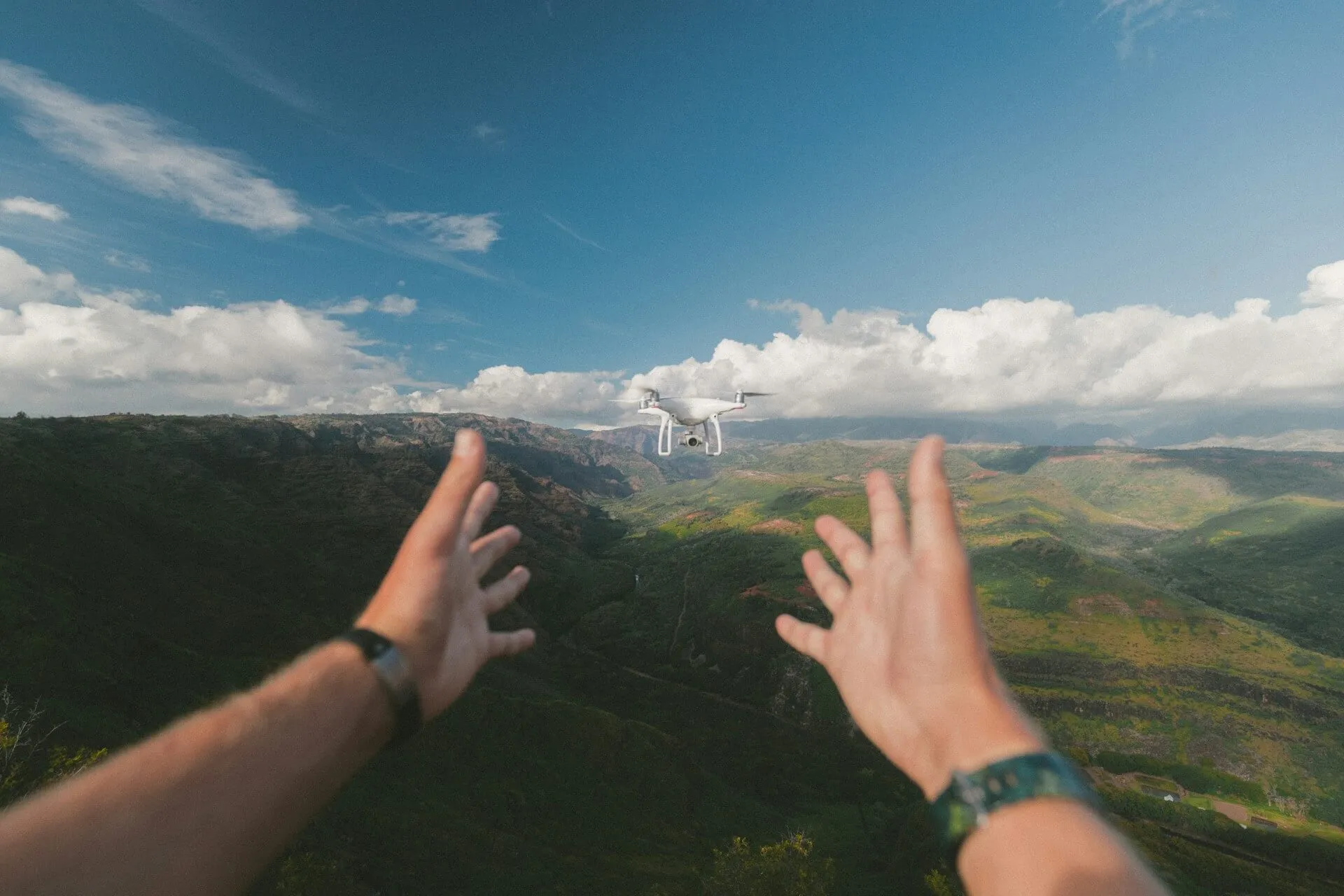 A man flying a white kite over a lush green hillside.