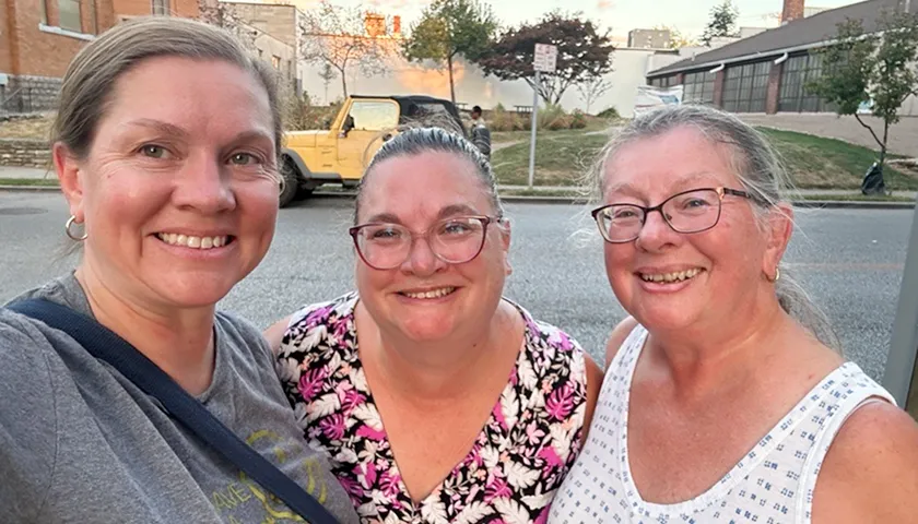 Three women standing next to each other on a street.