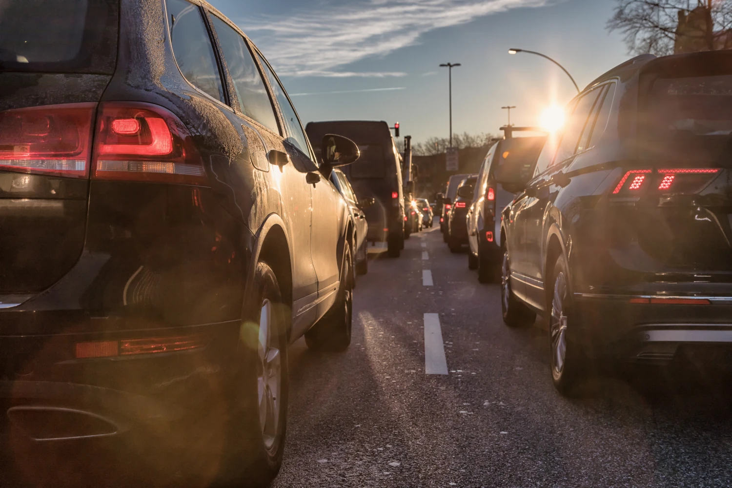 Traffic jam with cars lined up on a city street during sunset with sun glare.