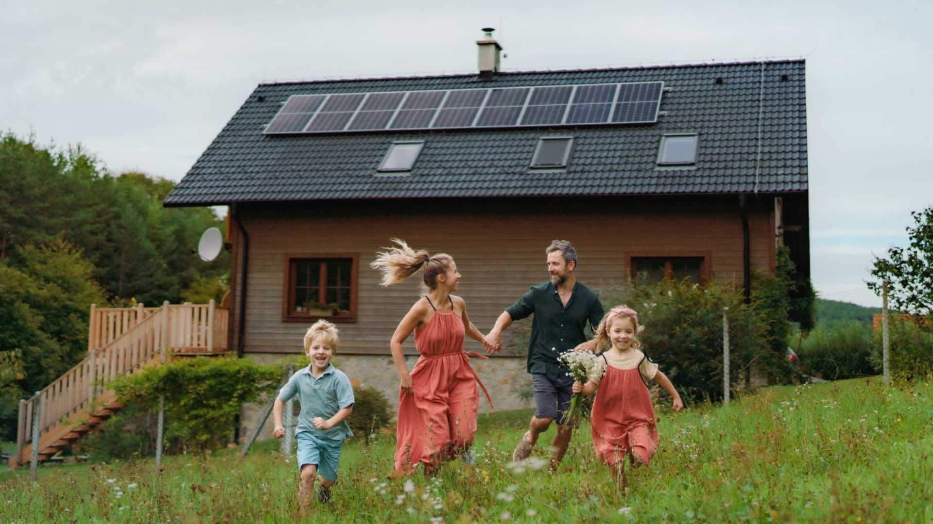 Junge Familie läuft lachend über eine Wiese vor einem Haus mit Solaranlage
