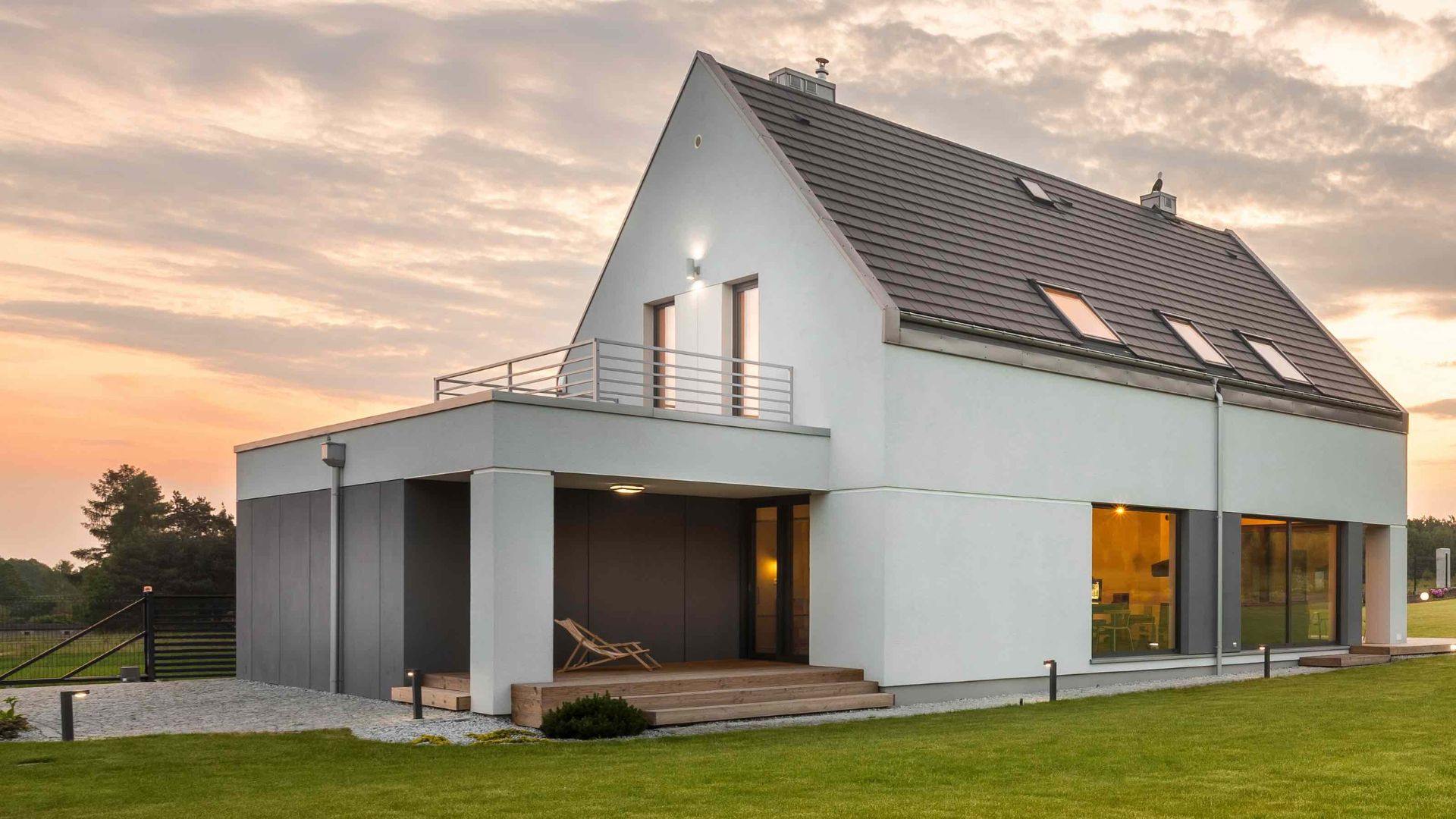 Modernes Einfamilienhaus mit Garten und Terrasse bei Sonnenuntergang.