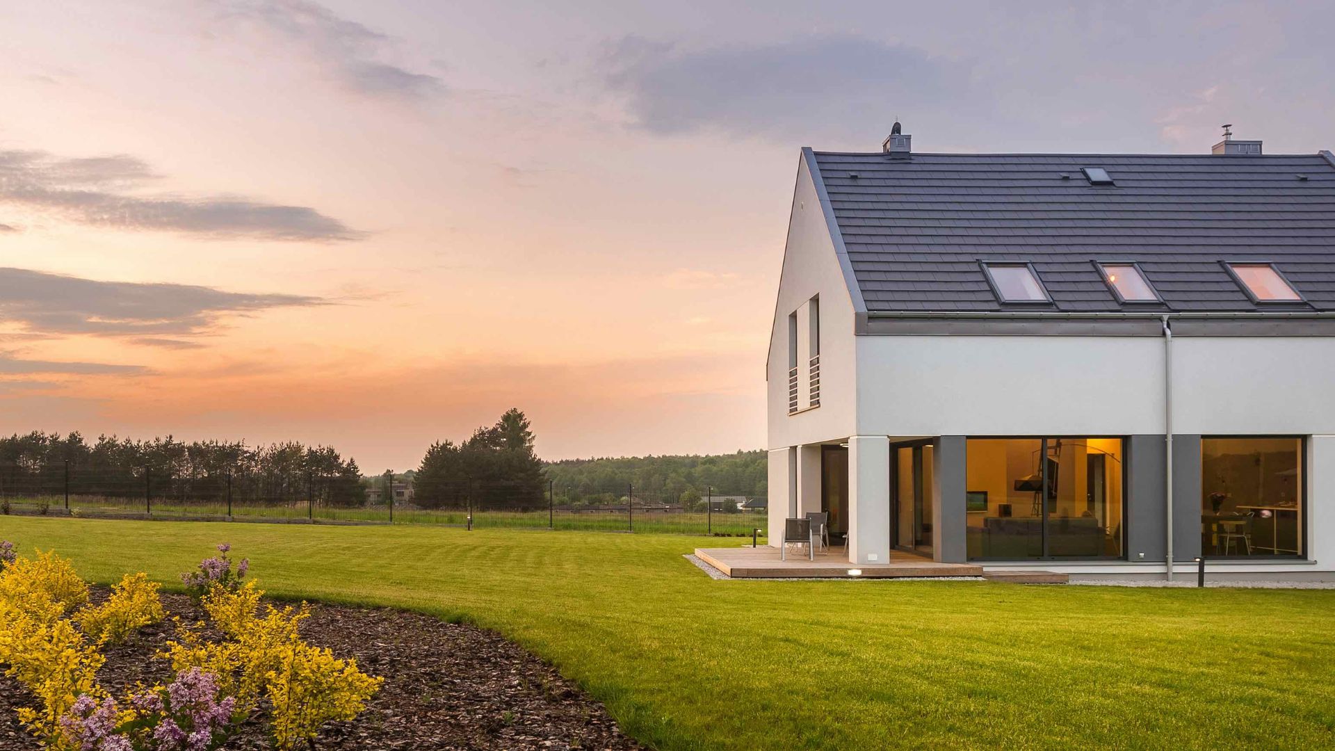 Modernes Einfamilienhaus auf dem Land bei Sonnenuntergang mit großem Garten