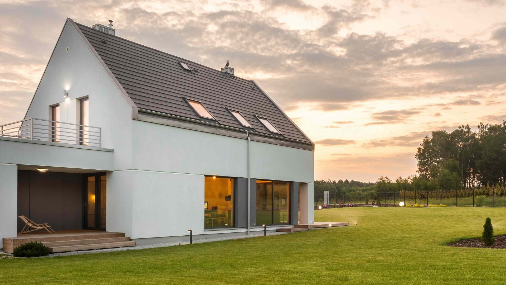 Modernes Einfamilienhaus mit großem Garten bei Sonnenuntergang.