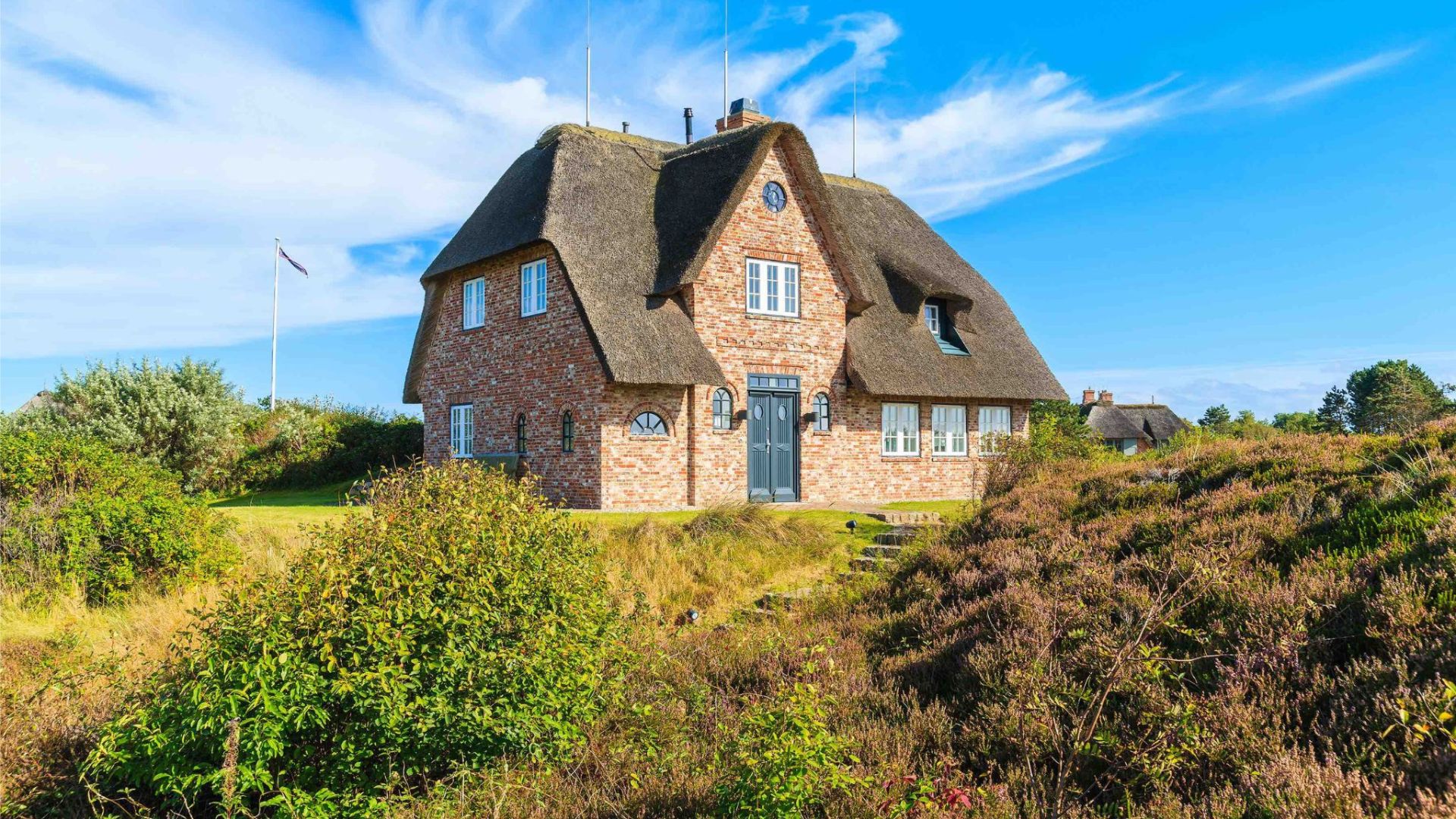 Traditionelles Backsteinhaus mit Reetdach inmitten einer Dünenlandschaft.