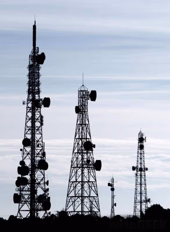 Silhouetted telecommunications towers against a cloudy sky, showcasing various heights and antenna configurations.