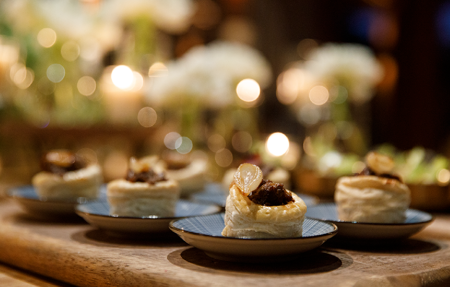 Close-up of small puff pastry appetizers topped with caramelized onion on blue-rimmed plates.