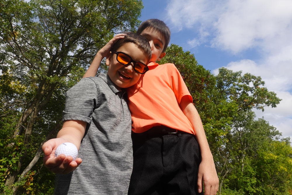 Dream Kid Declan poses with his brother, holding a golf ball and wearing orange sunglasses.