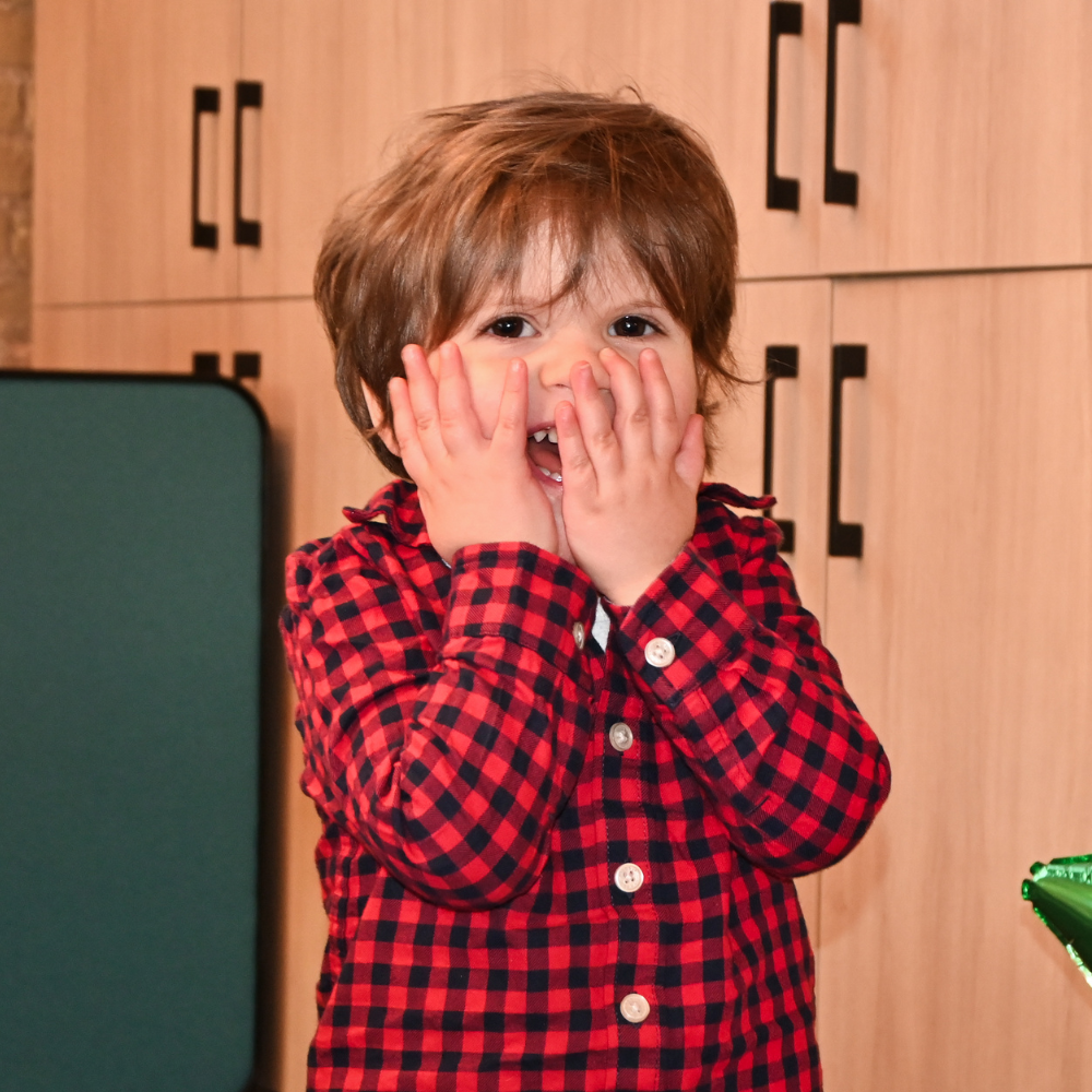 Dream Kid Beau covering his joyful smile with his hands, his eyes wide with excitement.