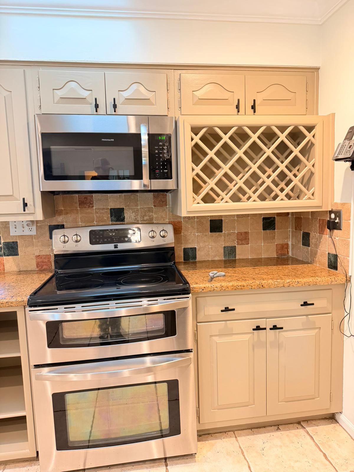 Kitchen area with stainless steel stove, microwave, beige cabinets, granite countertop, and tile backsplash.
