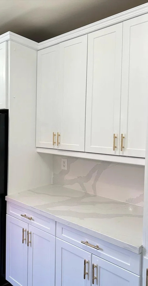 White kitchen cabinets with gold handles and a white marble countertop and backsplash.