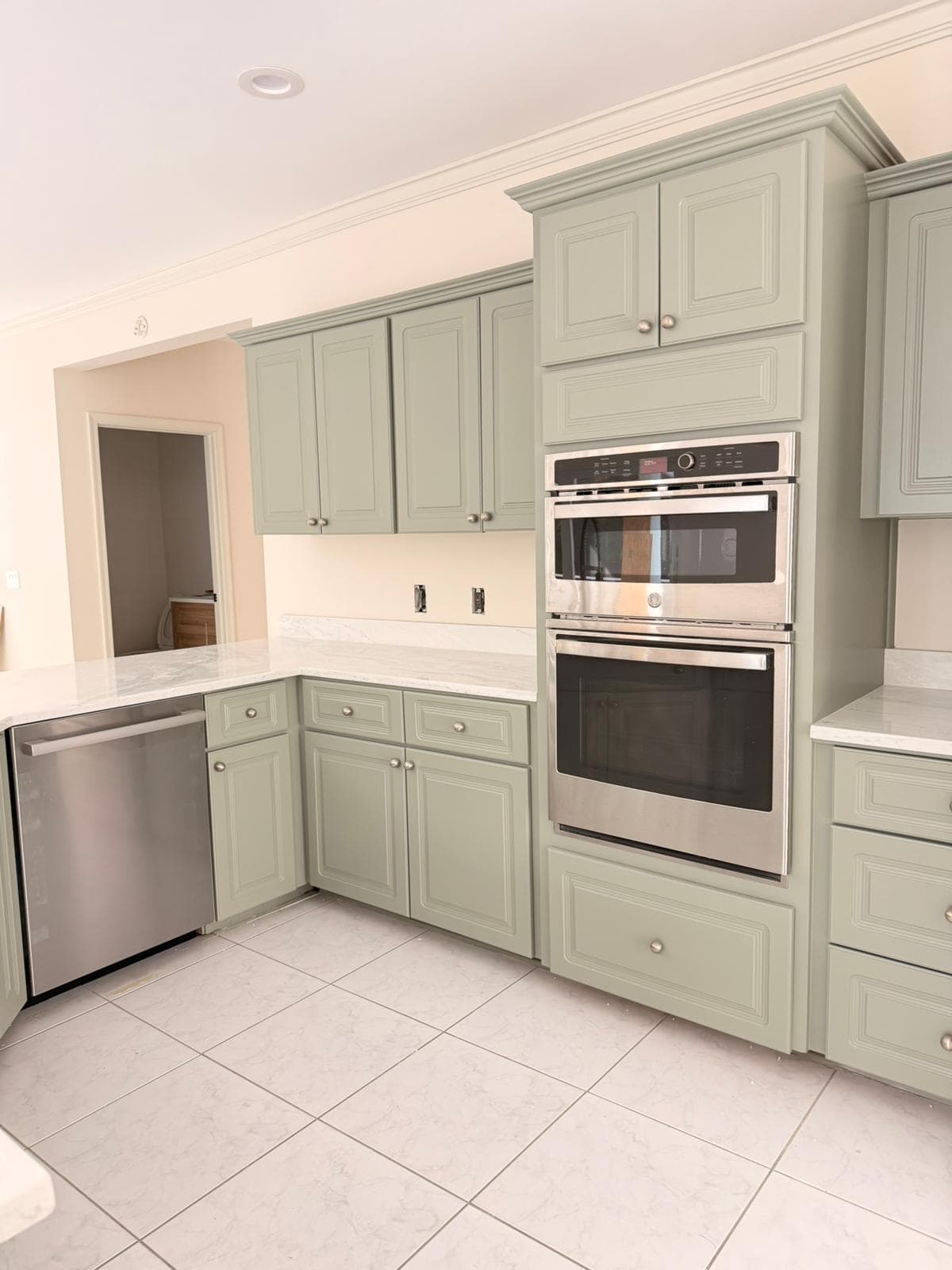 Modern kitchen corner with sage green cabinets, marble countertops, stainless steel oven and dishwasher.