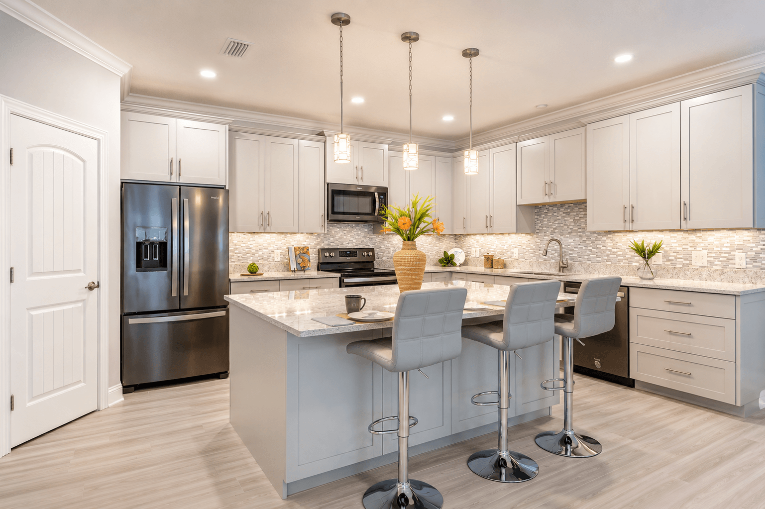 Modern kitchen with gray cabinets, marble island, stainless steel appliances, and three gray bar stools.
