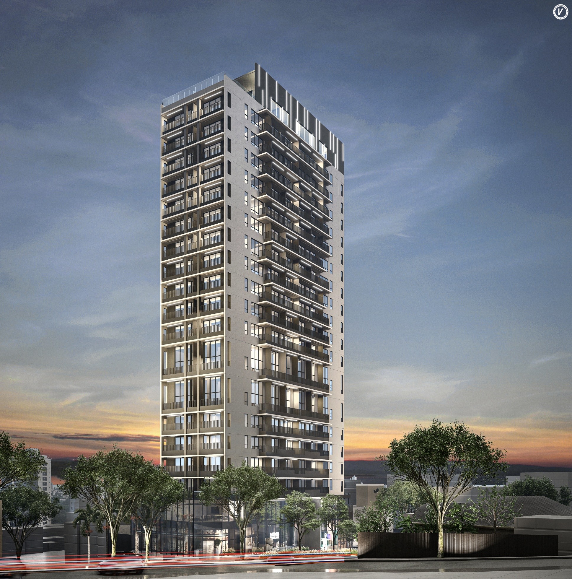 Tall modern apartment building illuminated at dusk with other buildings and trees under a cloudy sky.