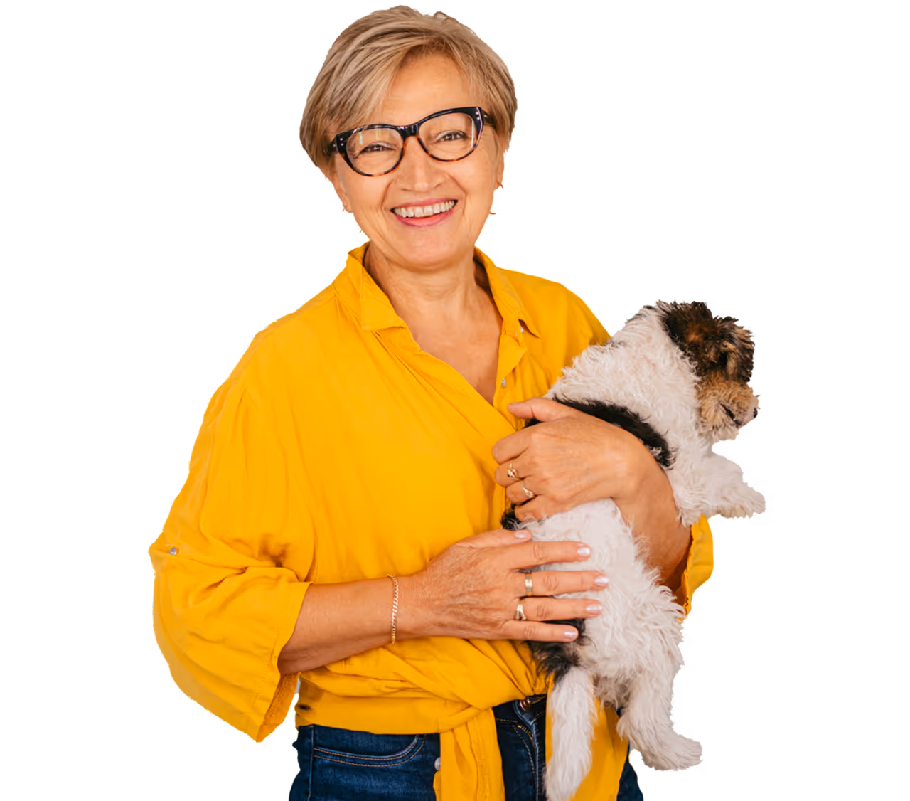 Smiling woman with glasses and a yellow blouse holding a small scruffy puppy against a white background.
