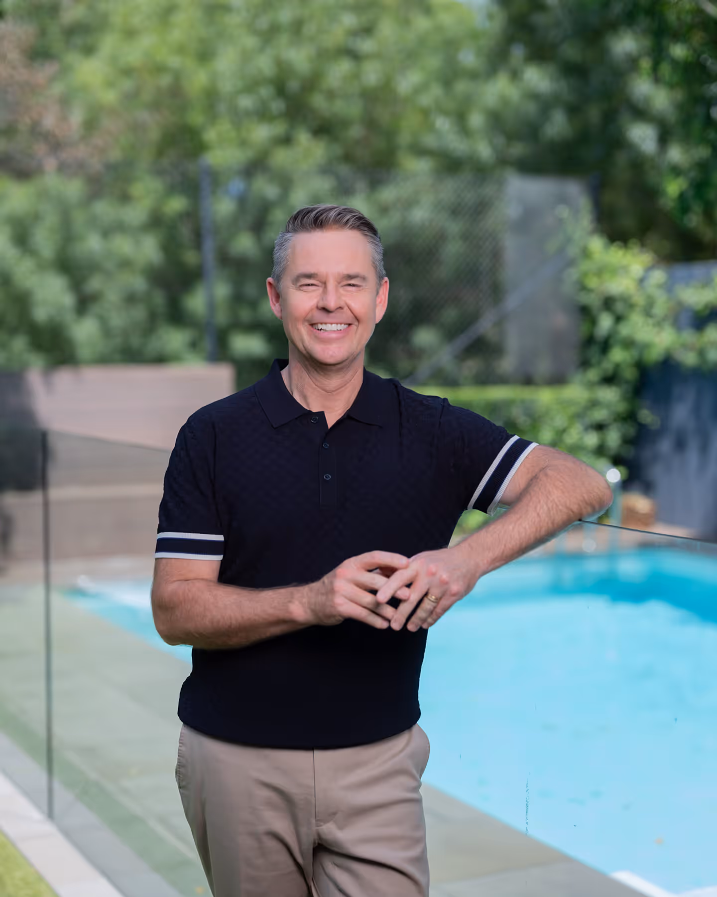 Portrait of Todd Woodbridge smiling outside in front of a backyard swimming pool.