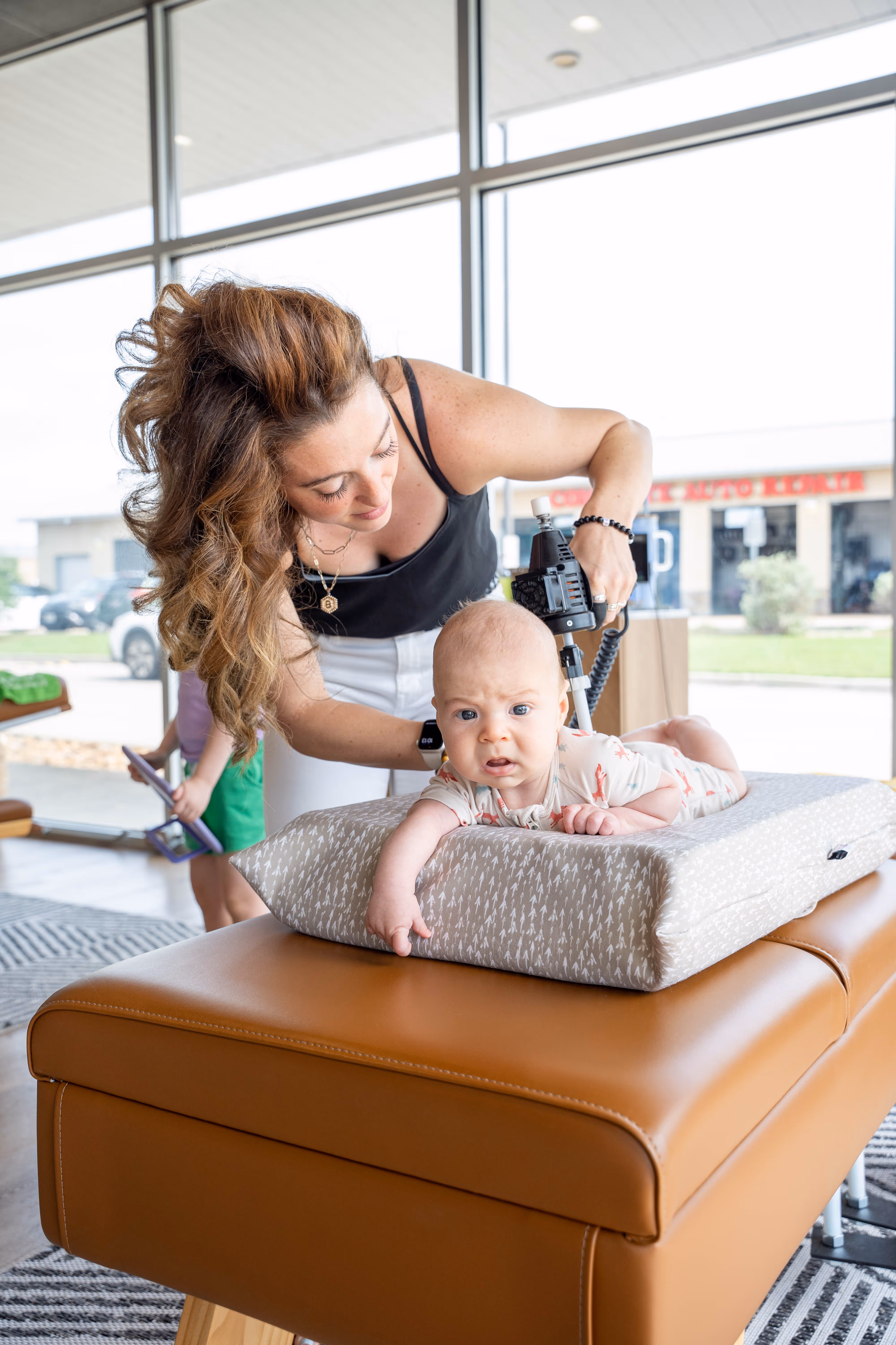 Young female chiropractor gently adjusts infant on cushioned table in bright clinic, showcasing safe prenatal chiropractic...
