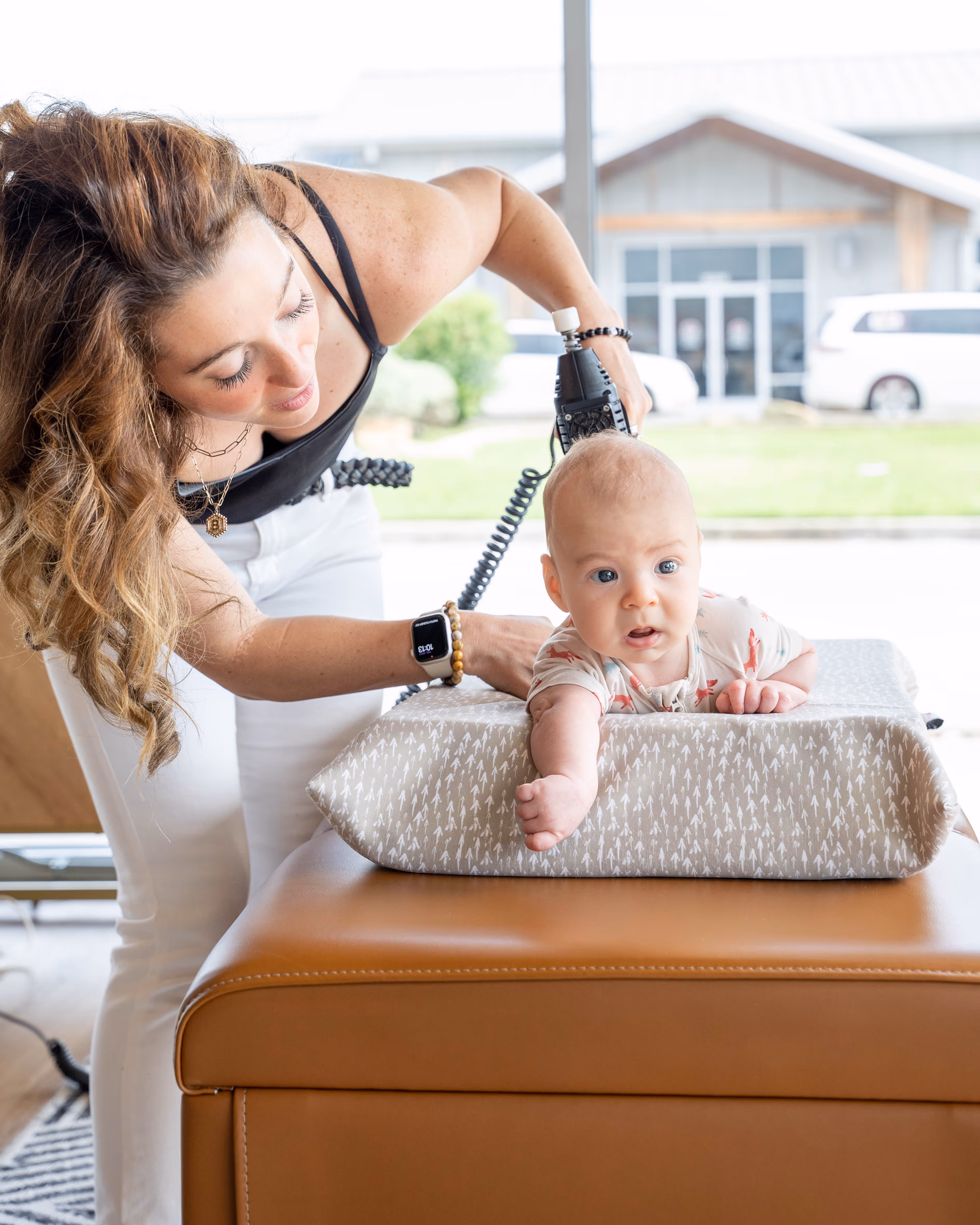 Chiropractor gently adjusts infant on cushioned table in bright room, showcasing prenatal chiropractic care benefits for m...
