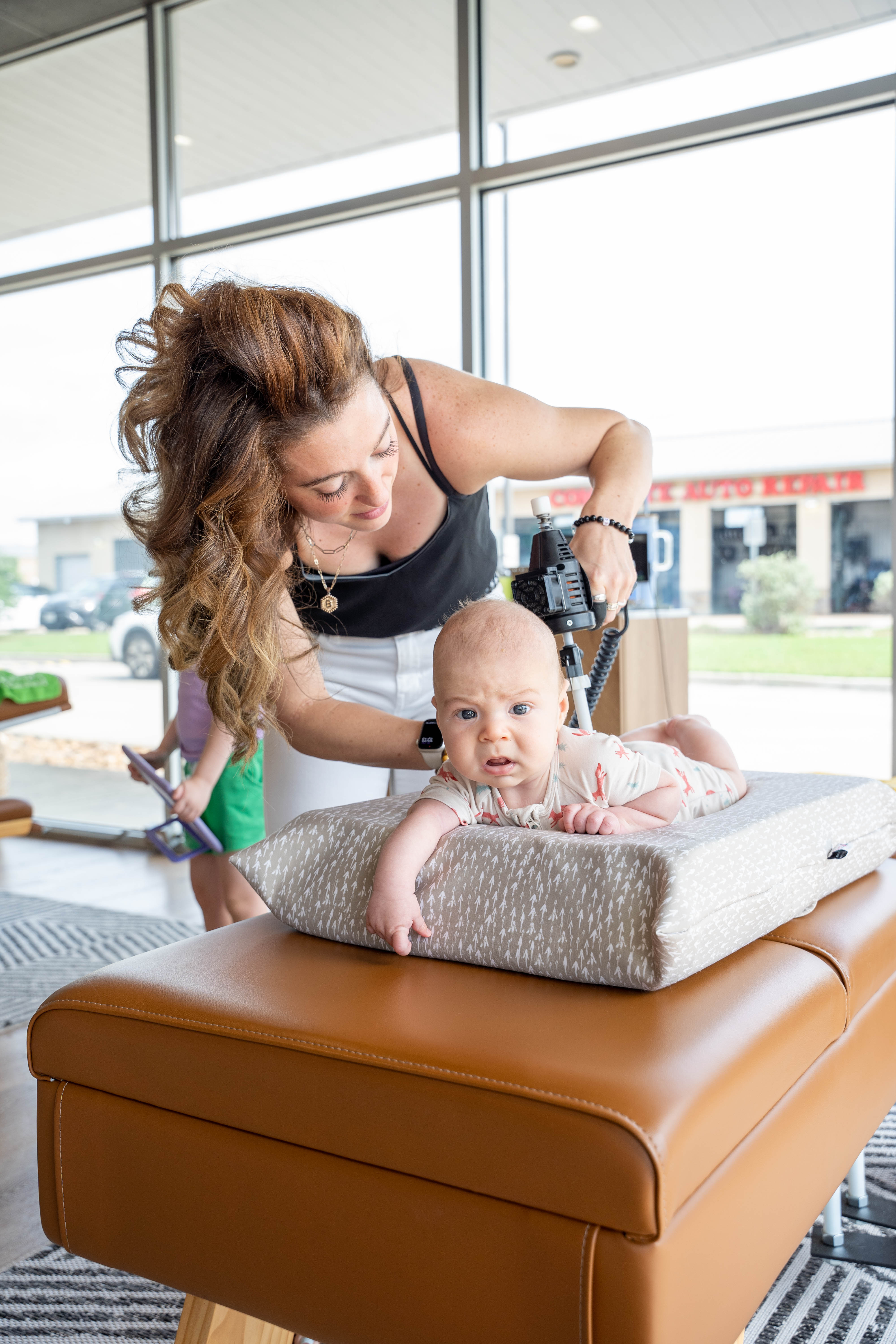 Young mother and infant receiving gentle chiropractic adjustment in bright clinic, promoting infant chiropractic care and ...