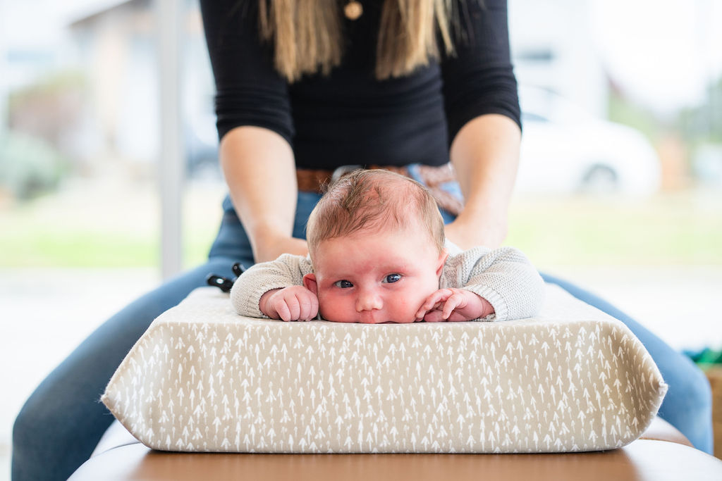 Young mother receiving infant chiropractic care on cushioned table in bright room, promoting holistic health for babies.