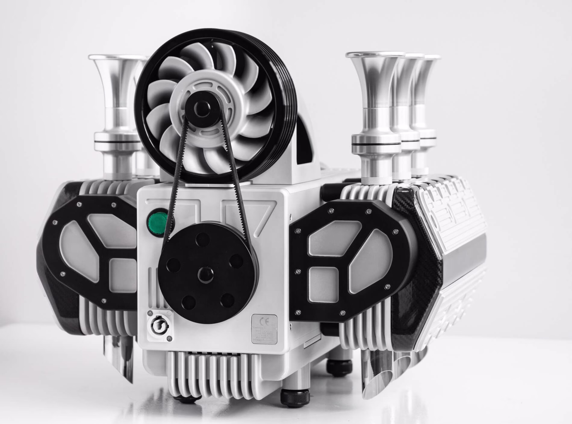 Close-up of a silver and black mechanical engine with pulleys and cylindrical components on a white surface.