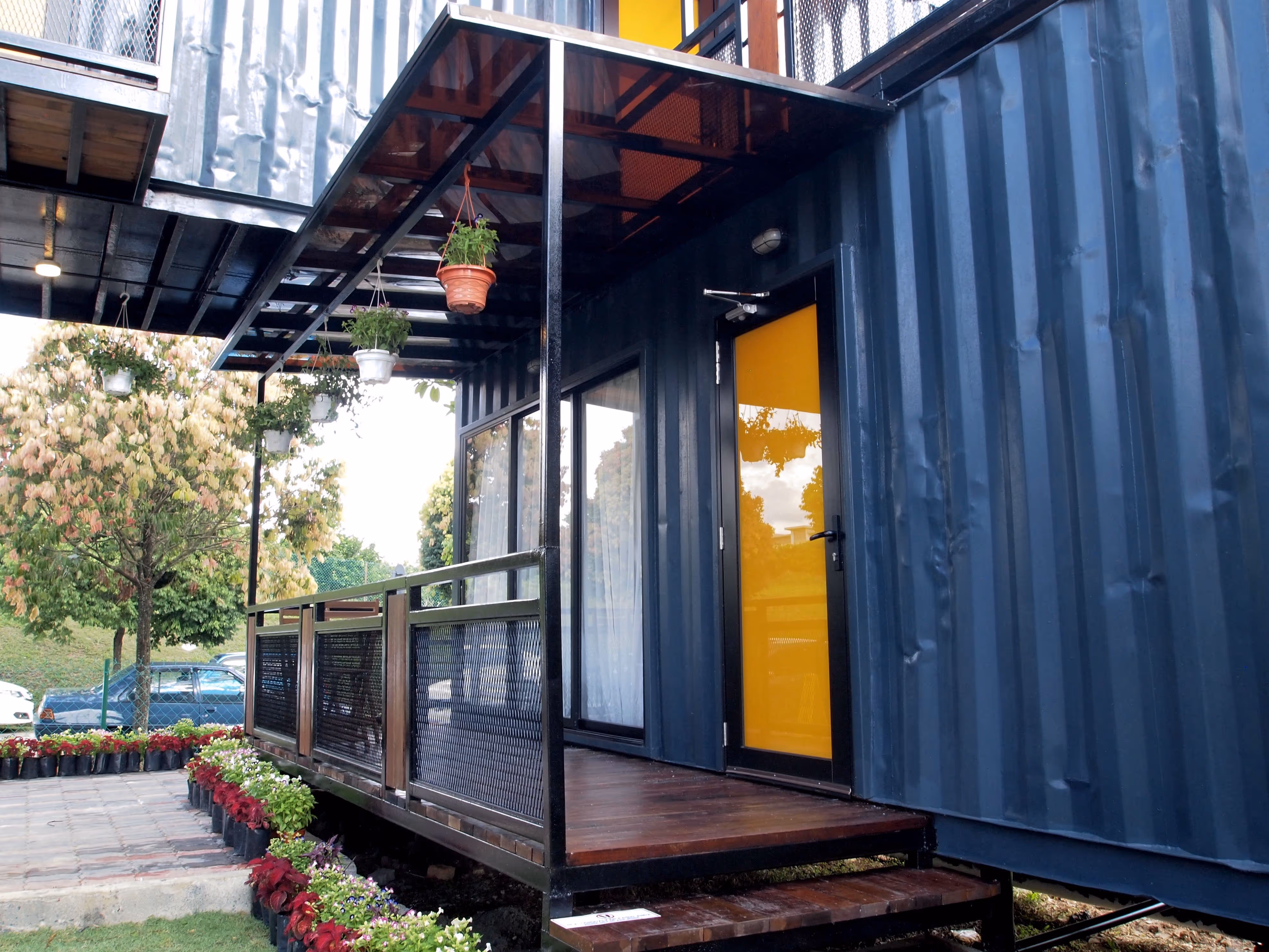 A blue shipping container with a yellow door and a potted plant on the deck.