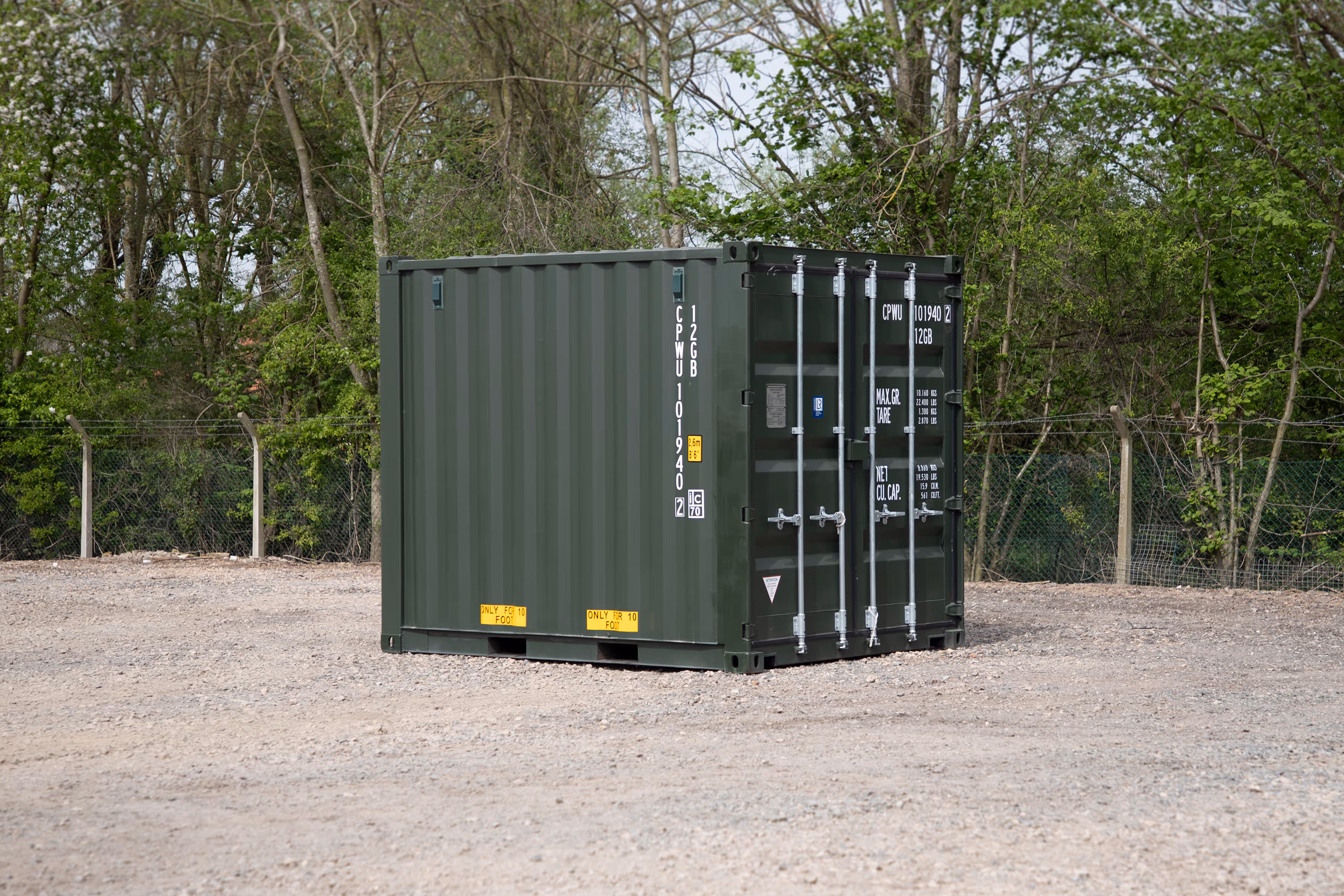 A large green shipping container is parked in a gravel lot.