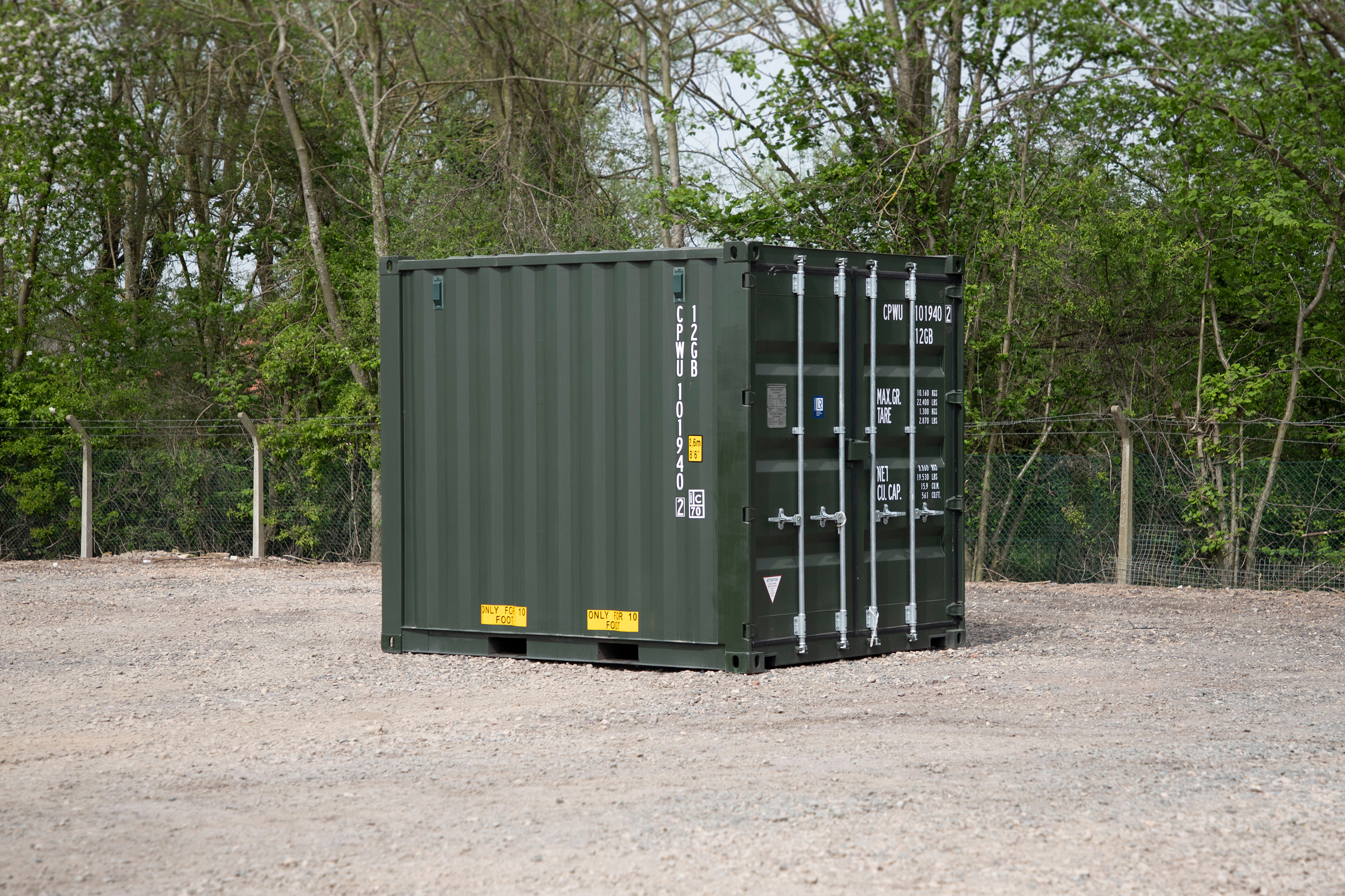 A large green shipping container is parked in a gravel lot.