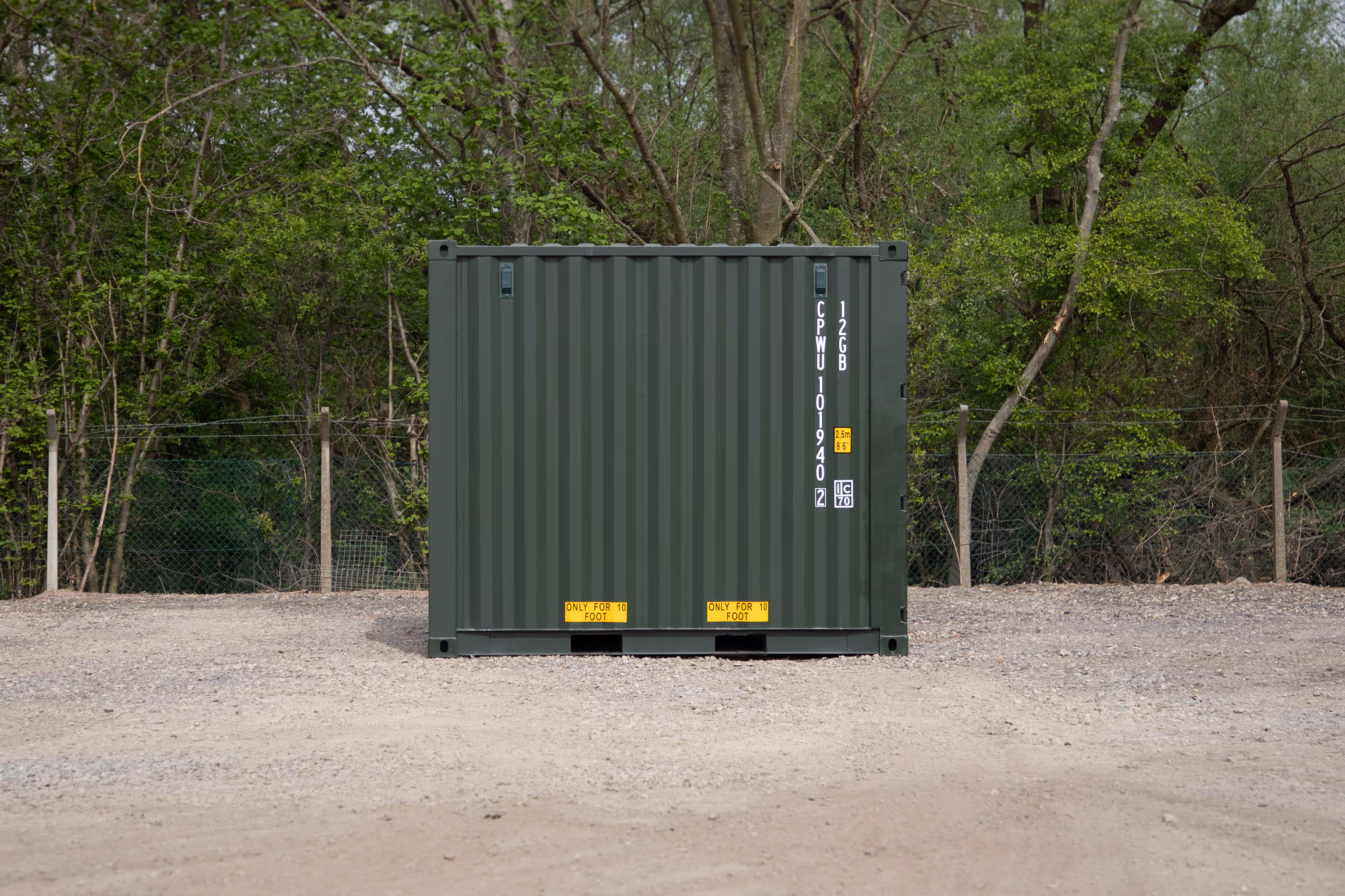 A large green shipping container sits in a dirt lot.