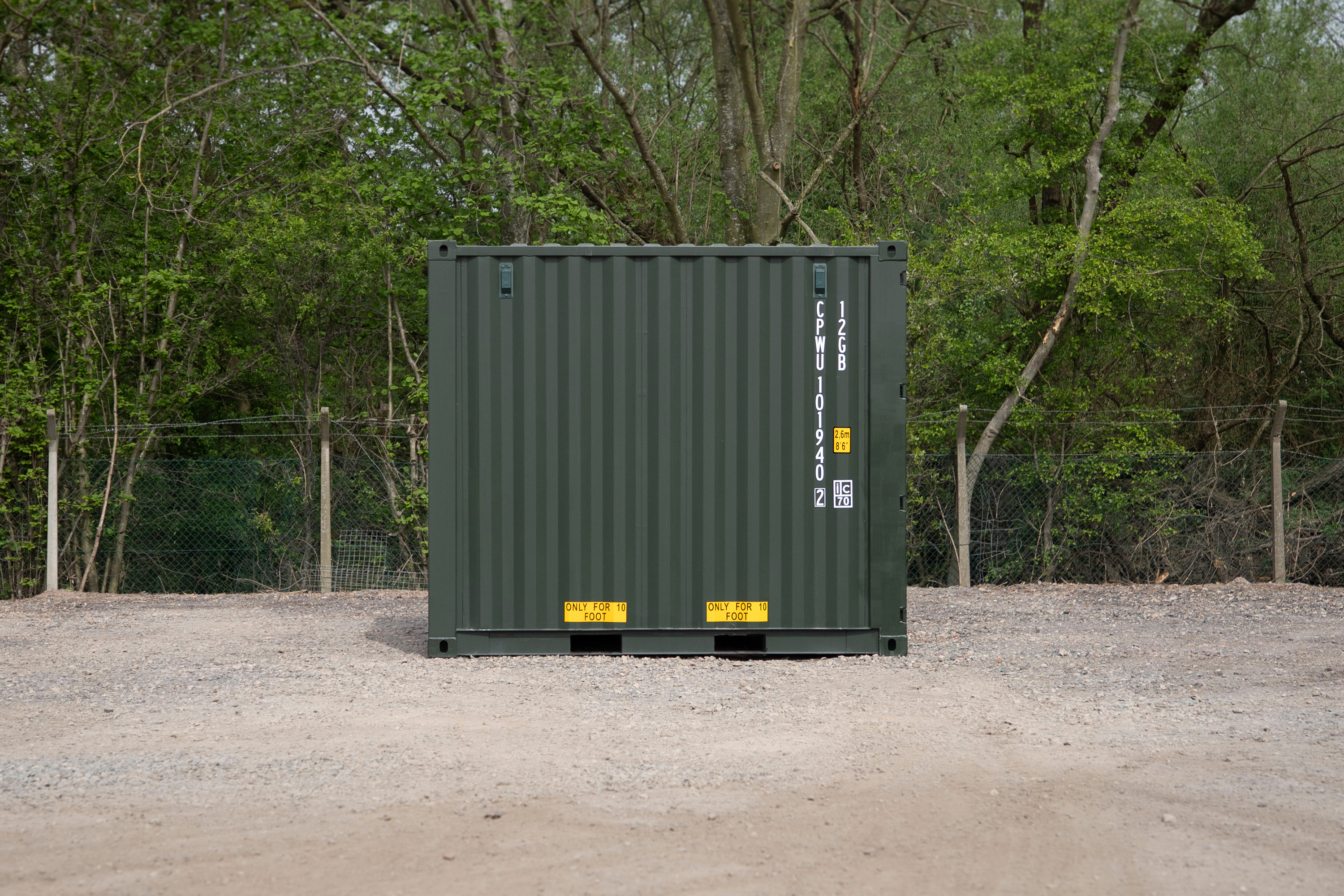 A large green shipping container sits in a dirt lot.