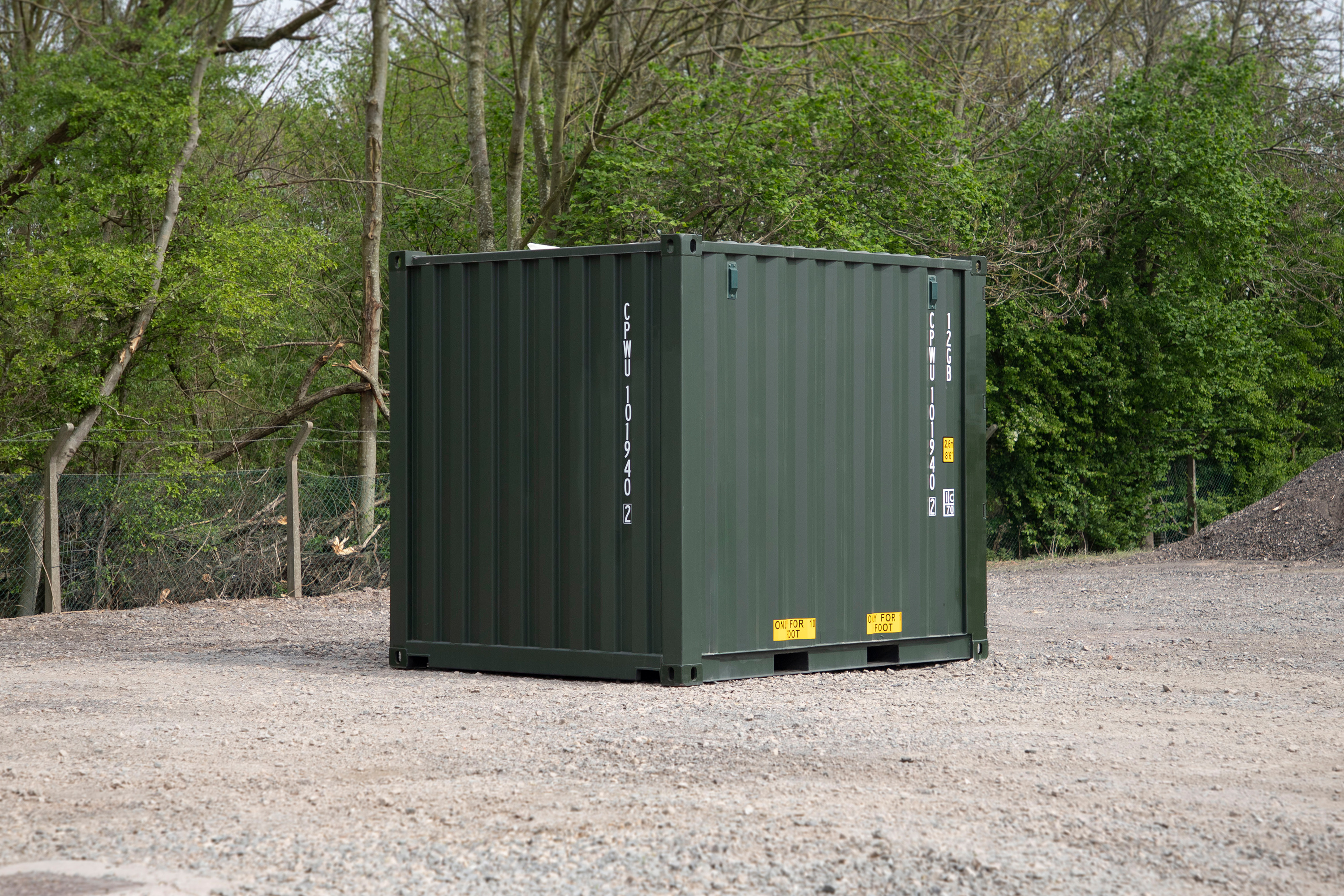 A green shipping container is sitting in a gravel lot.