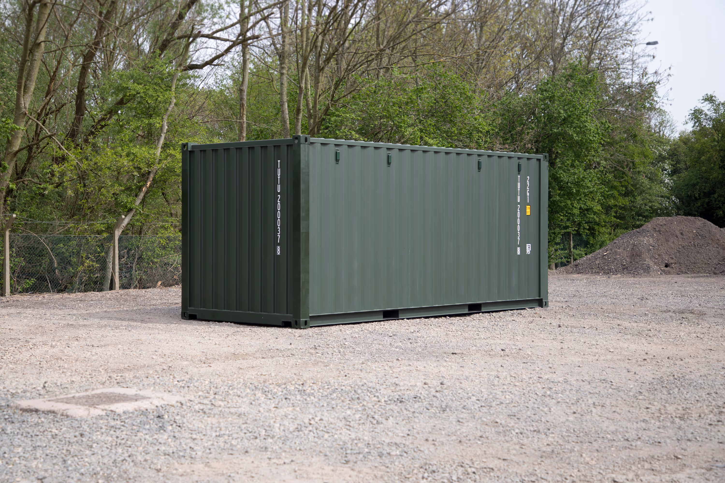 A large green shipping container sits in a gravel lot.