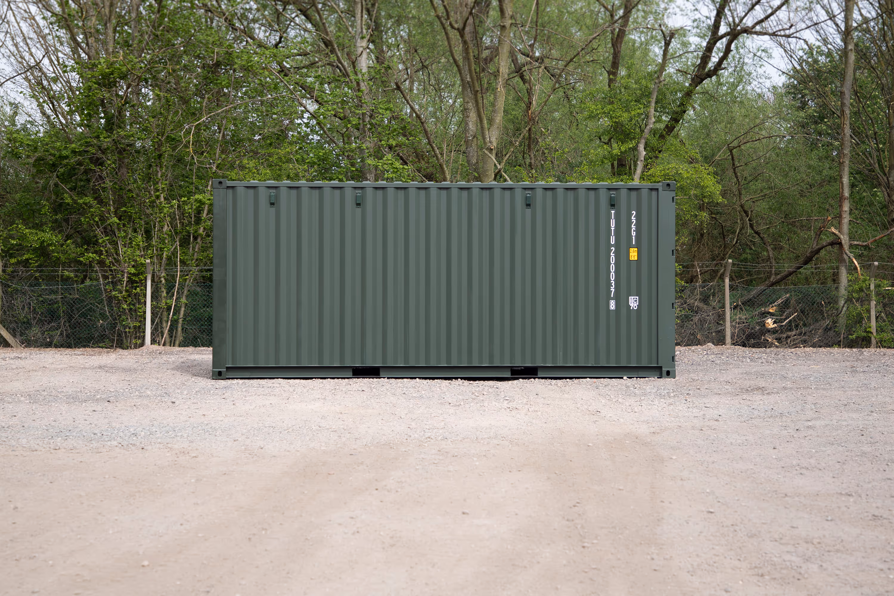A large green shipping container is parked in a dirt lot.