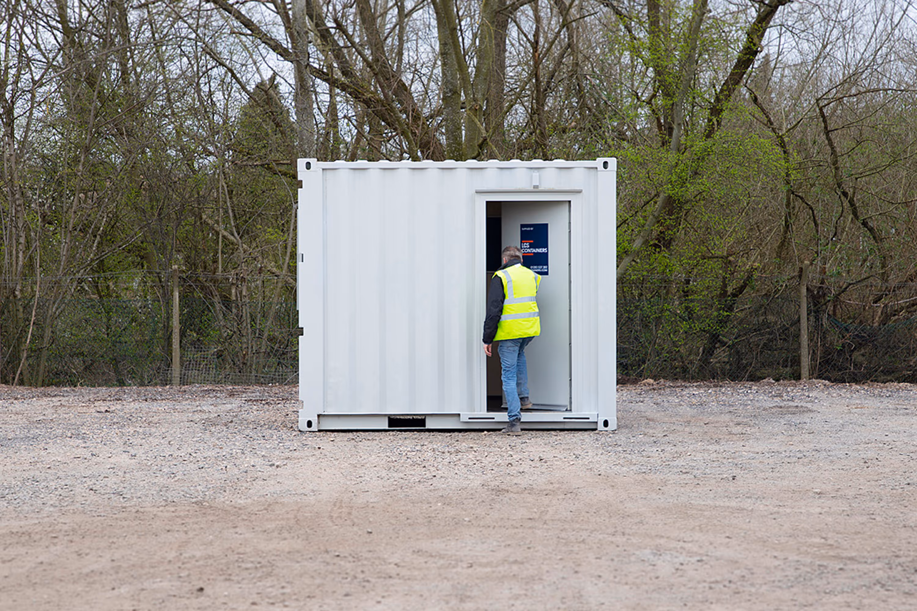 A man in a yellow vest is standing in front of a white shipping container.