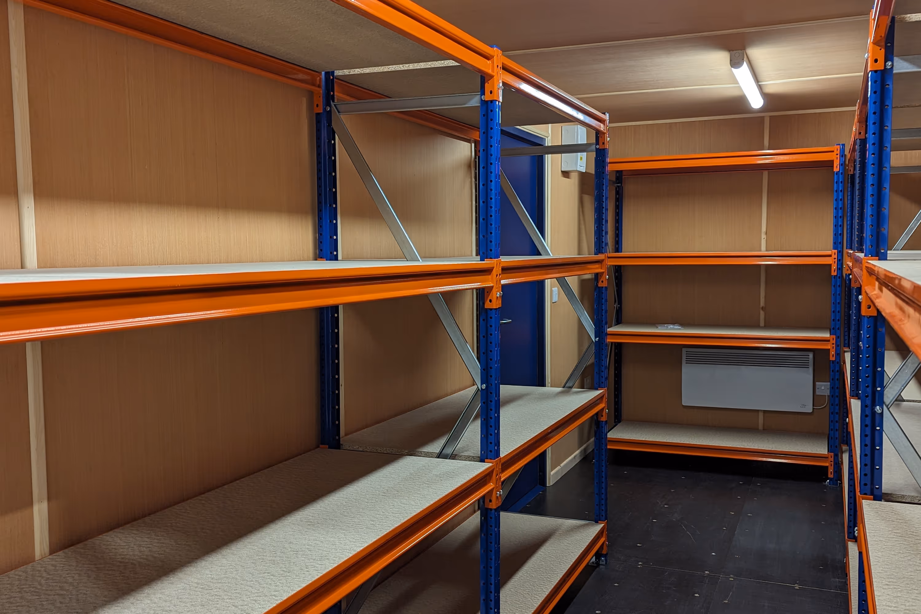 A storage room in a shipping container with shelves and a blue door.