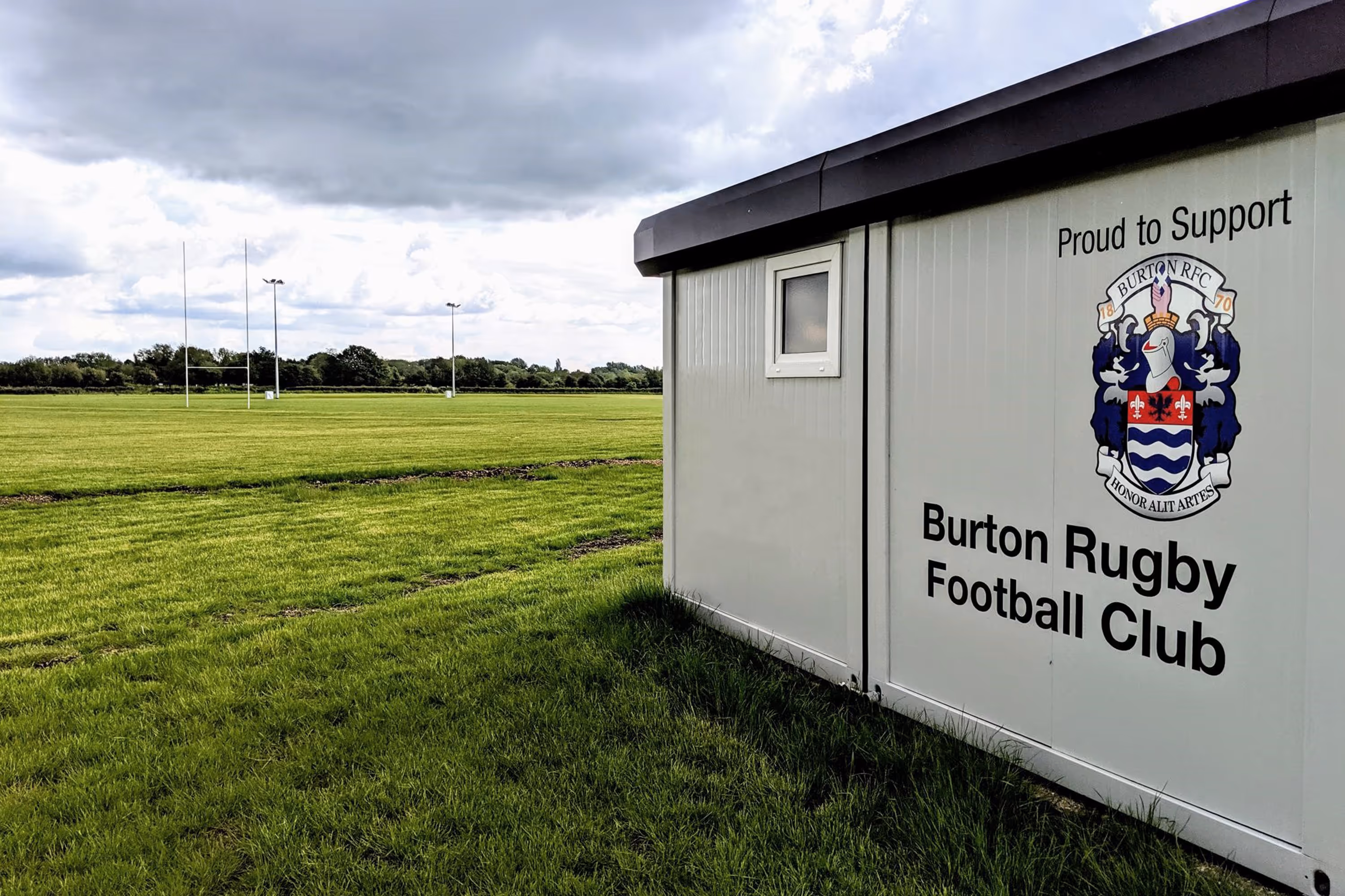 A white building with a black roof and a sign that says Burton Rugby Club.