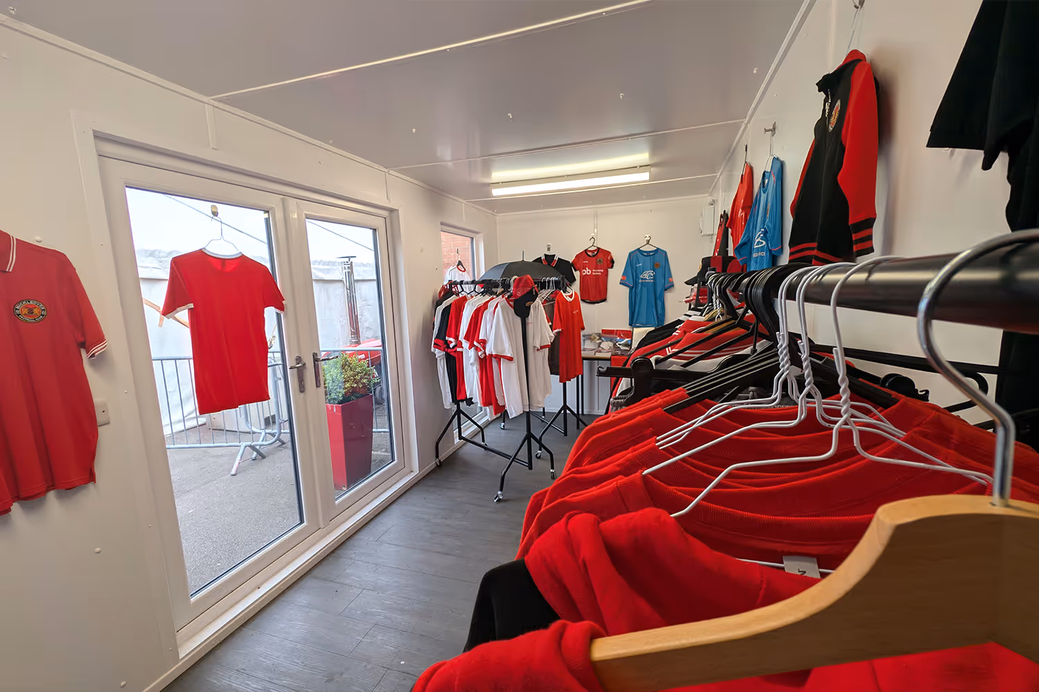 Small retail space with sportswear on hangers and racks, featuring red and blue football shirts and jackets.