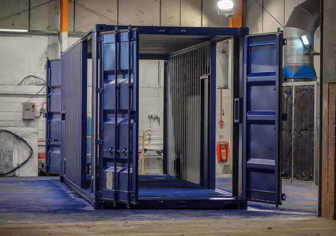 Empty blue shipping container with open doors inside a warehouse.