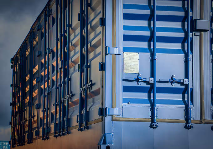 Close-up of blue shipping container doors with locking bars and a warning label in soft evening light.