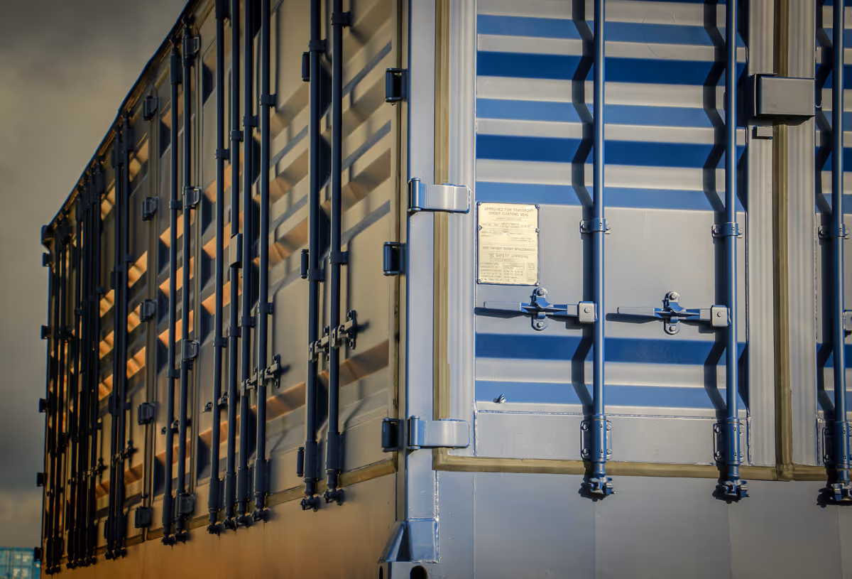 Close-up view of the rear corner of a blue shipping container with metal locking bars and a posted label.