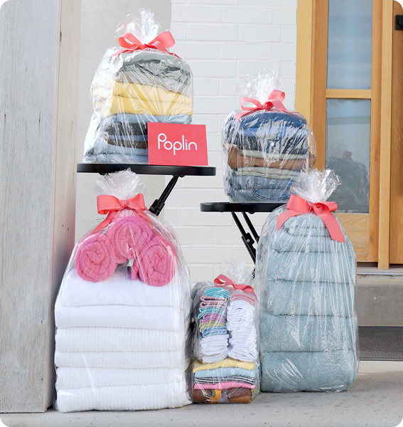 Stacks of folded laundry in clear bags with pink bows and a Poplin card, arranged by a front door.