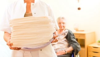 Woman carrying neatly folded laundry with a senior in the background, representing the return of clean, finished laundry that pickup and delivery service provides