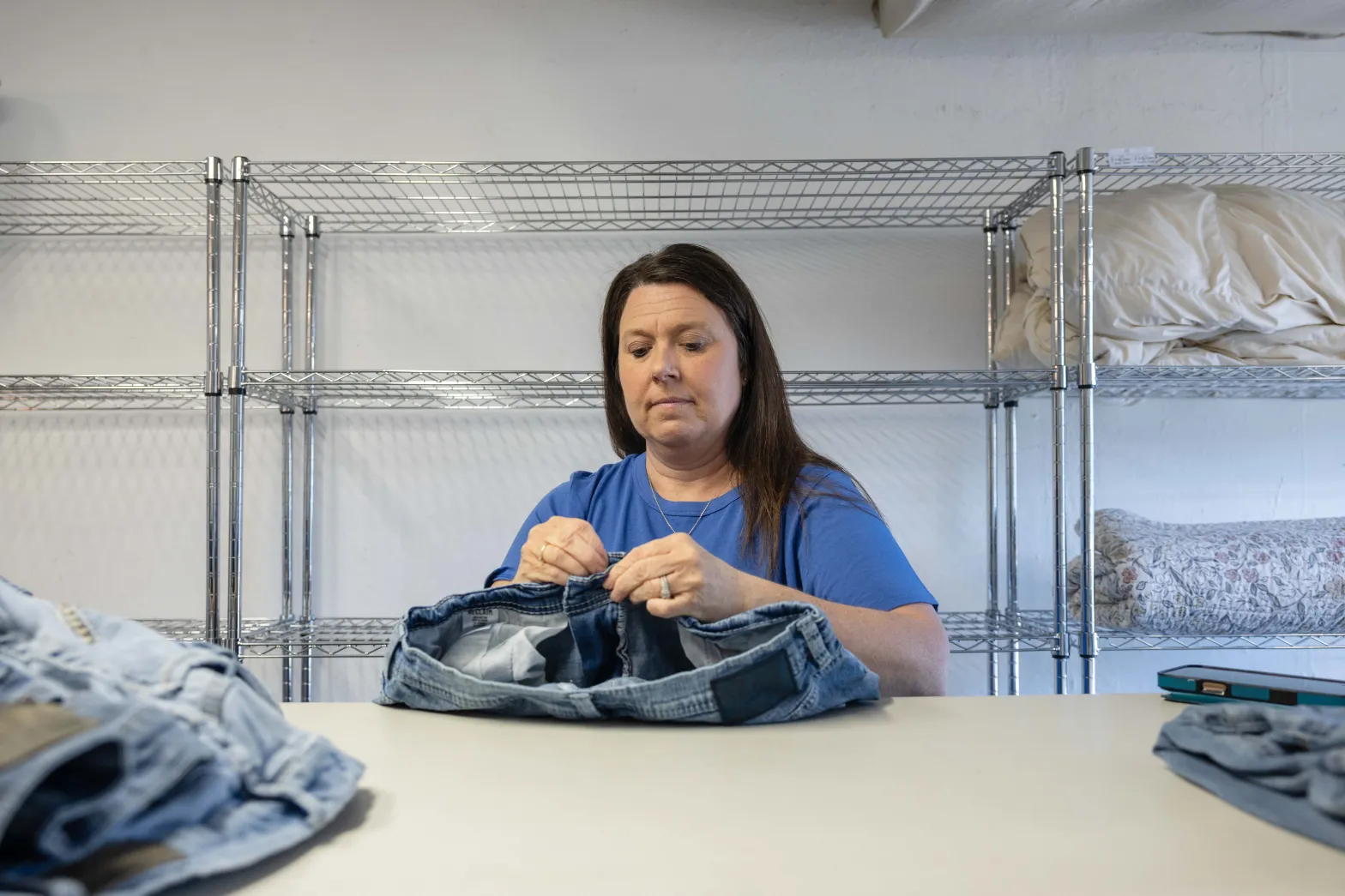 A woman working with a pair of jeans at a folding or packing table.