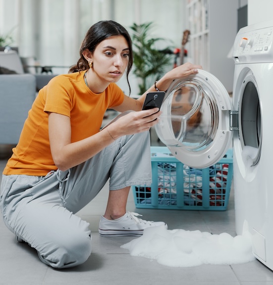 Woman pausing to check her phone mid-laundry, illustrating how competing demands interrupt even the small windows set aside to get it done