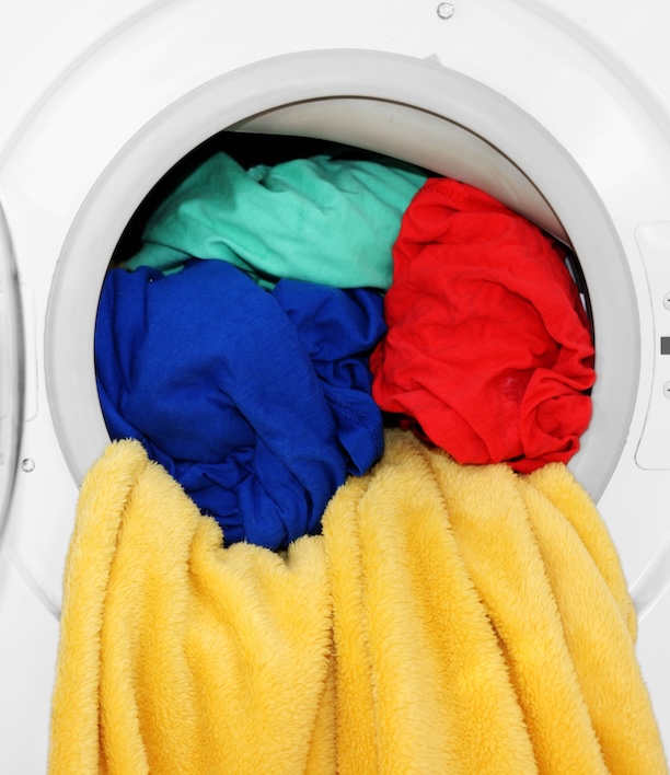 Open washing machine filled with colorful laundry, representing the recurring cycle that this guide helps you decide whether it makes sense to hand off