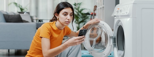 Woman pausing to check her phone mid-laundry, illustrating how competing demands interrupt even the small windows set aside to get it done