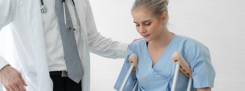 Woman receiving mobility guidance from a medical professional in a hospital setting, representing the recovery period during which laundry restrictions are in place and household tasks still need handling