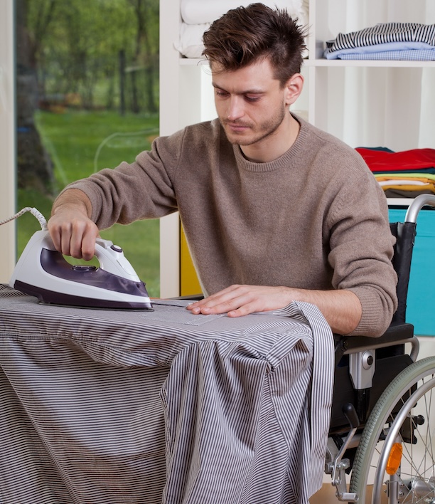 Person in a wheelchair ironing clothes, representing the physical challenges laundry tasks present for people managing disabilities or mobility limitations