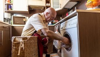 Older man bending down to reach a front-loading washing machine, illustrating the physical demands laundry places on seniors and the risk those demands quietly carryYou said: I need a title tag, meta description and alt text for the hero image for this webpage.
