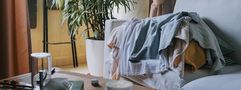 Pile of laundry on a couch in an apartment with warm interior lighting in the background, representing the weekly logistics problem of living without in-unit machines